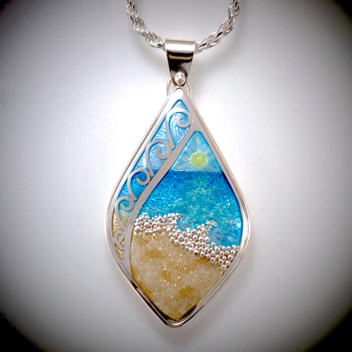 Beach theme enamel pendant necklace with sand, waves, blue aqua water, and sun on the horizon. Hangs on silver chain