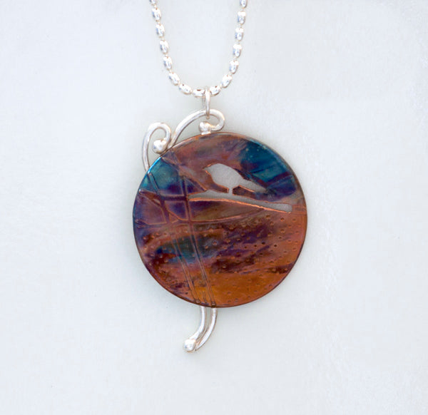 Flame painted copper pendant necklace with silhouette of bird on branch, silver twigs in background