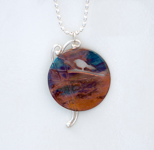 Flame painted copper pendant necklace with silhouette of bird on branch, silver twigs in background