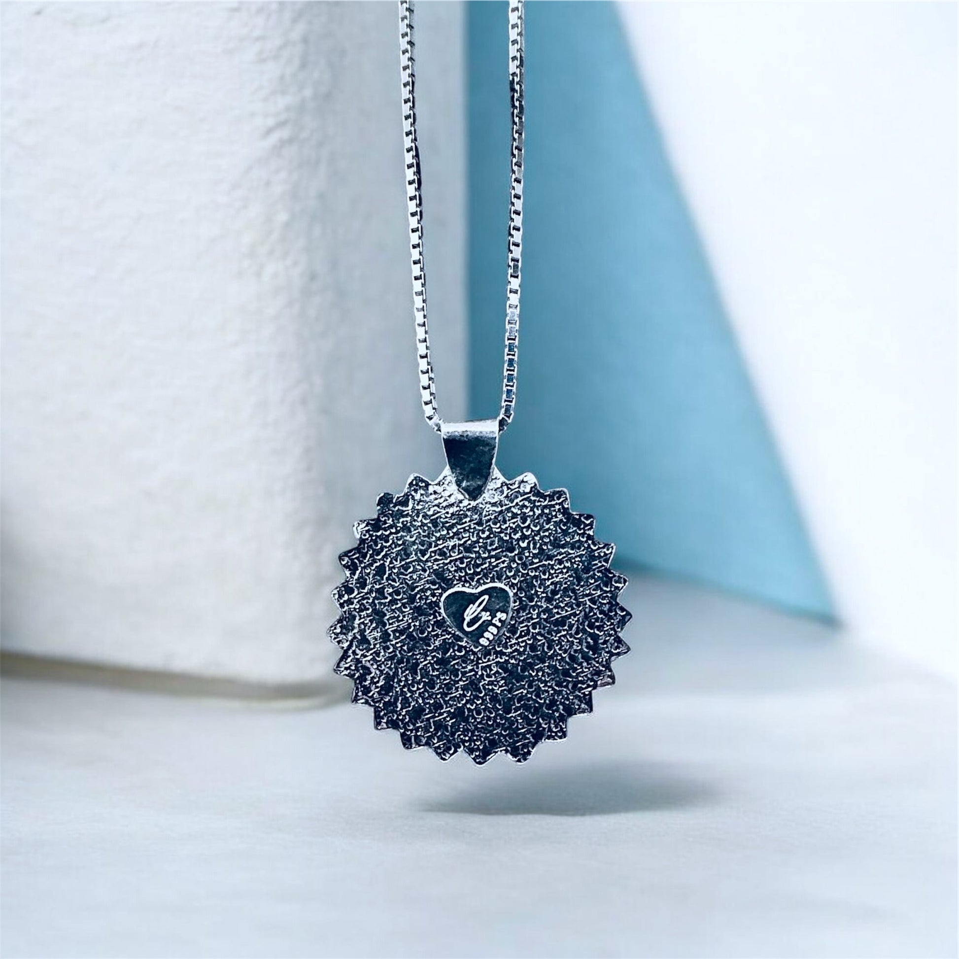 Back side of silver necklace with a textured pendant on a light background