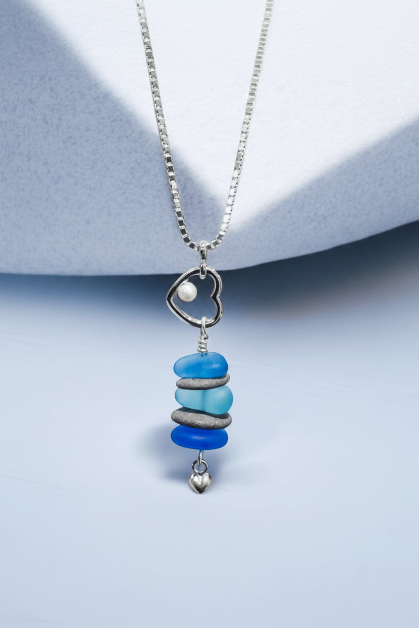 Beach lovers heart pendant necklace with beach stones and blue glass on a light blue background