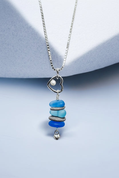 Beach lovers heart pendant necklace with beach stones and blue glass on a light blue background