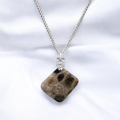 Necklace with a geometric-shaped Petoskey stone pendant with cubic zirconia square bail on a white background