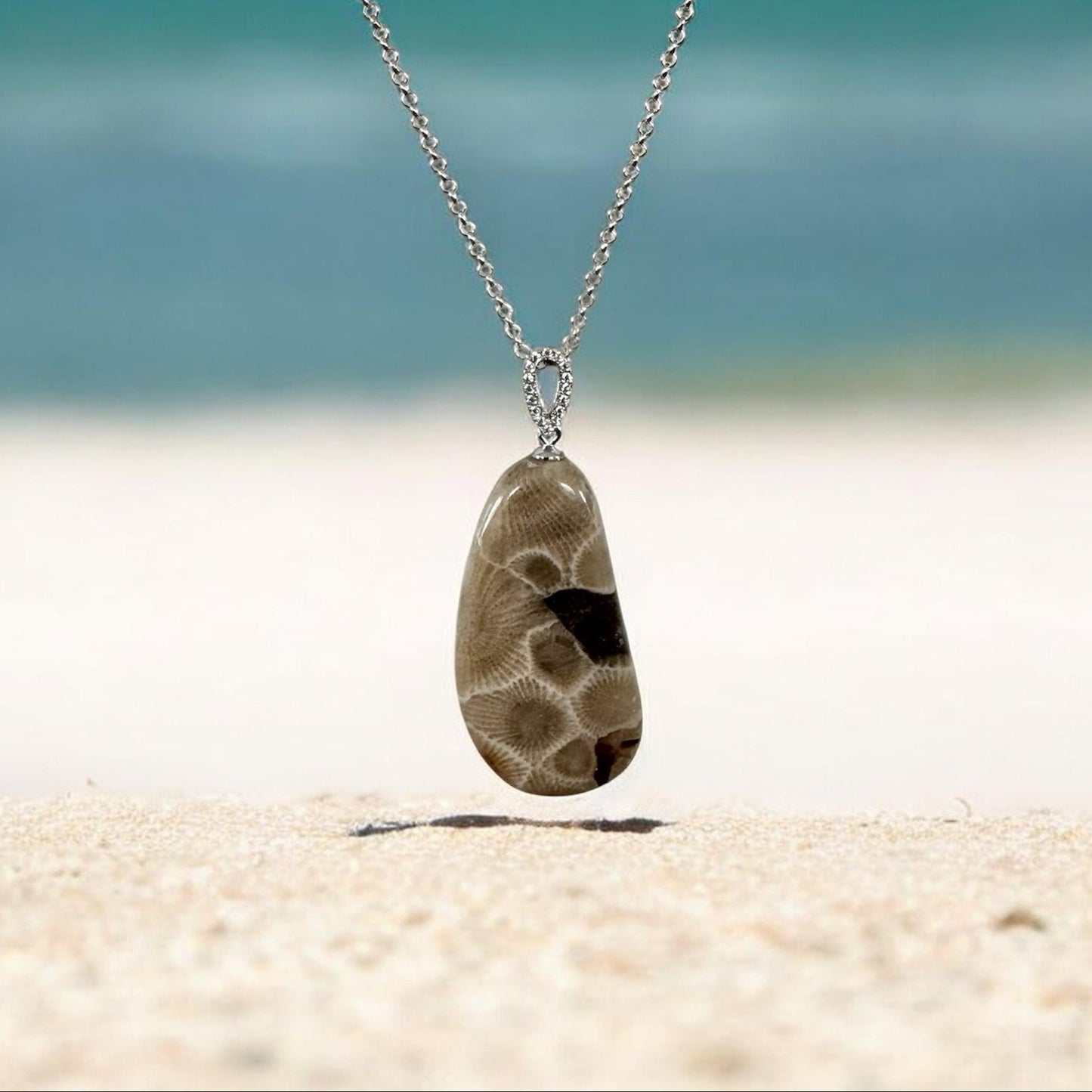 Necklace with a Petoskey stone pendant on a sandy beach Lake Michigan in the background