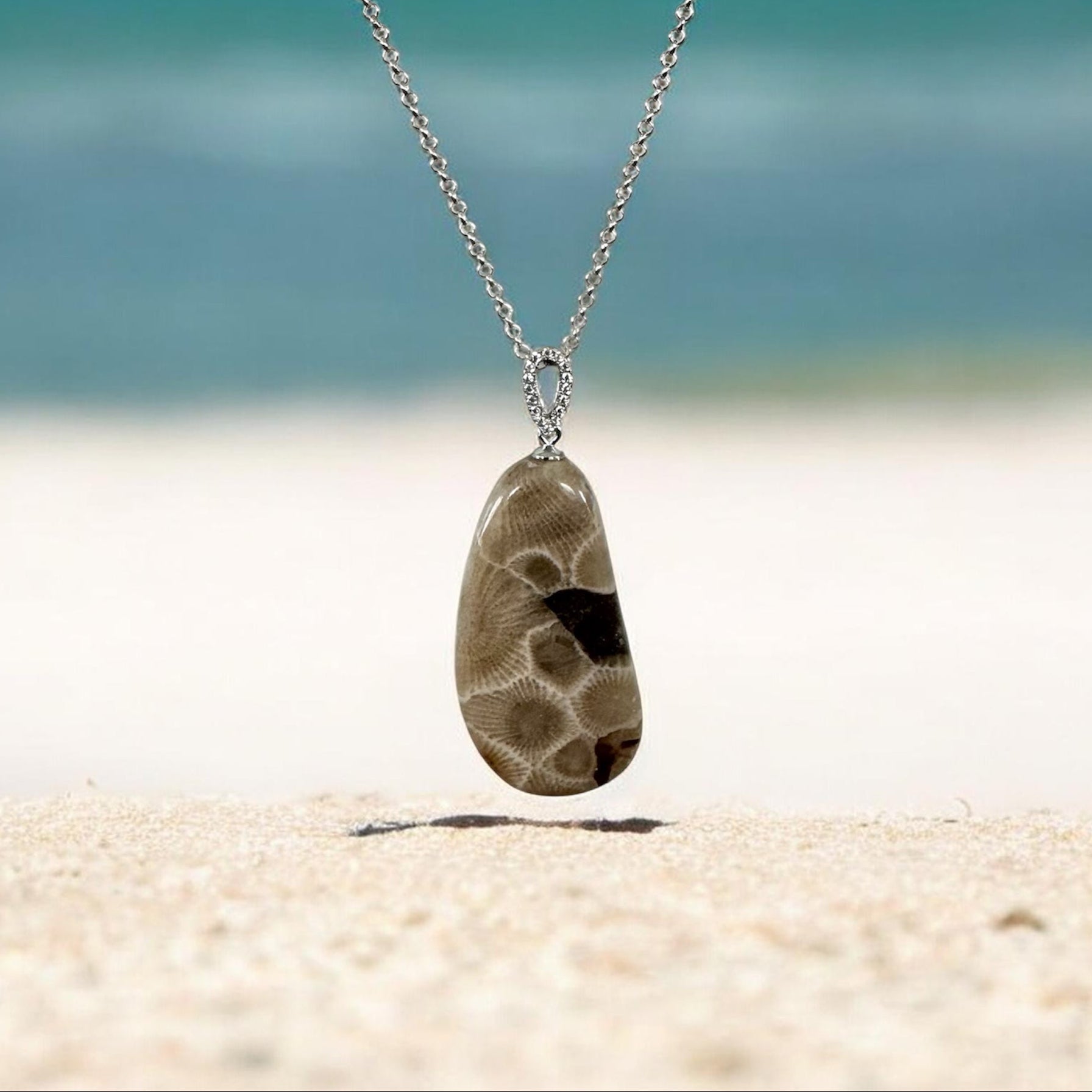 Necklace with a Petoskey stone pendant on a sandy beach Lake Michigan in the background