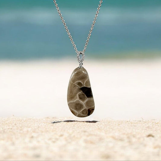 Necklace with a Petoskey stone pendant on a sandy beach Lake Michigan in the background