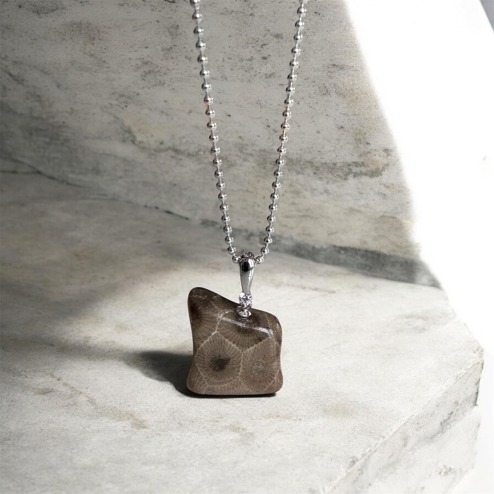 Silver bead chain necklace with a petoskey stone pendant in the shape of a bear standing on a marble surface
