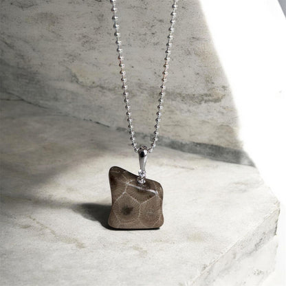 Silver bead chain necklace with a petoskey stone pendant in the shape of a bear standing on a marble surface