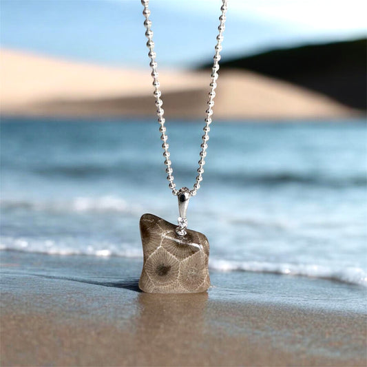 Necklace with a petoskey stone pendant on a sandy beach with Lake Michigan waves and sand dunes in the background